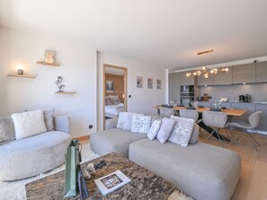 A modern living room with a sofa, coffee table, and a dining area with chairs and a table. - Elegant apartment, panoramic view, mountain - 7 guests (Huez)