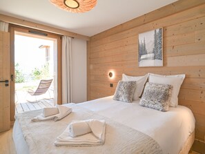 A bedroom with a large bed, a wooden wall, a painting, and a view of the outside. - Elegant apartment, panoramic view, mountain - 7 guests (Huez)