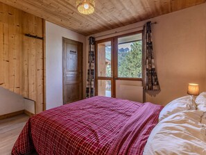 A bedroom with a wooden ceiling, a bed with a red checkered bedspread, a window with curtains, and a lamp on the bedside table. - Chalet with panoramic view - 14 guests (La Plagne 1800)