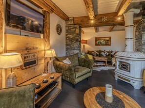 A cozy living room with a stone wall, a wooden ceiling, a fireplace, a television, and a sofa. - Chalet with panoramic view - 14 guests (La Plagne 1800)