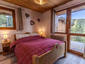 Ein Schlafzimmer mit einem Holzbett, zwei Nachttischen, einem Fenster mit Vorhängen und Blick auf eine Holzhütte.