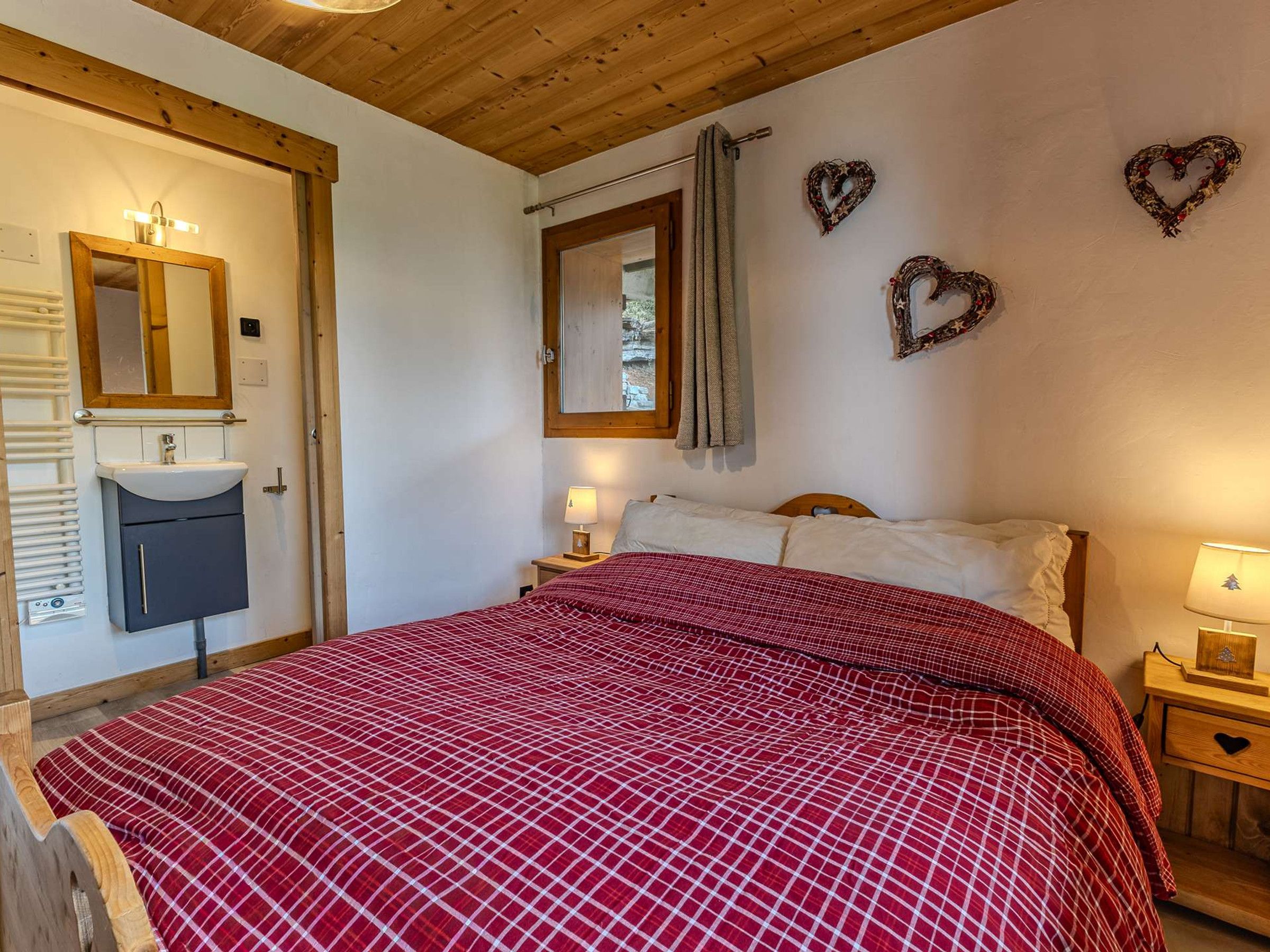 Een slaapkamer met een bed, een nachtkastje met een lamp, een spiegel, een wandverwarmer en een raam met gordijnen.