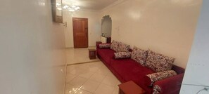 A living room with a red sofa, patterned cushions, a wooden door, and a tiled floor. - 2-Bedroom Apartment in Downtown Rabat (Rabat)