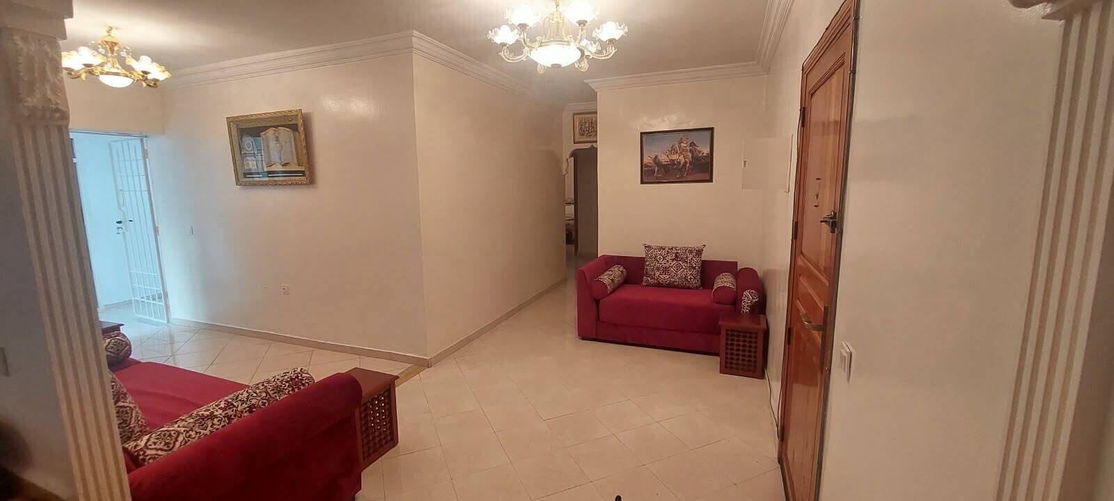 Ein Wohnzimmer mit einem roten Sofa, einem gemusterten Zierkissen und einer Chandelüster.