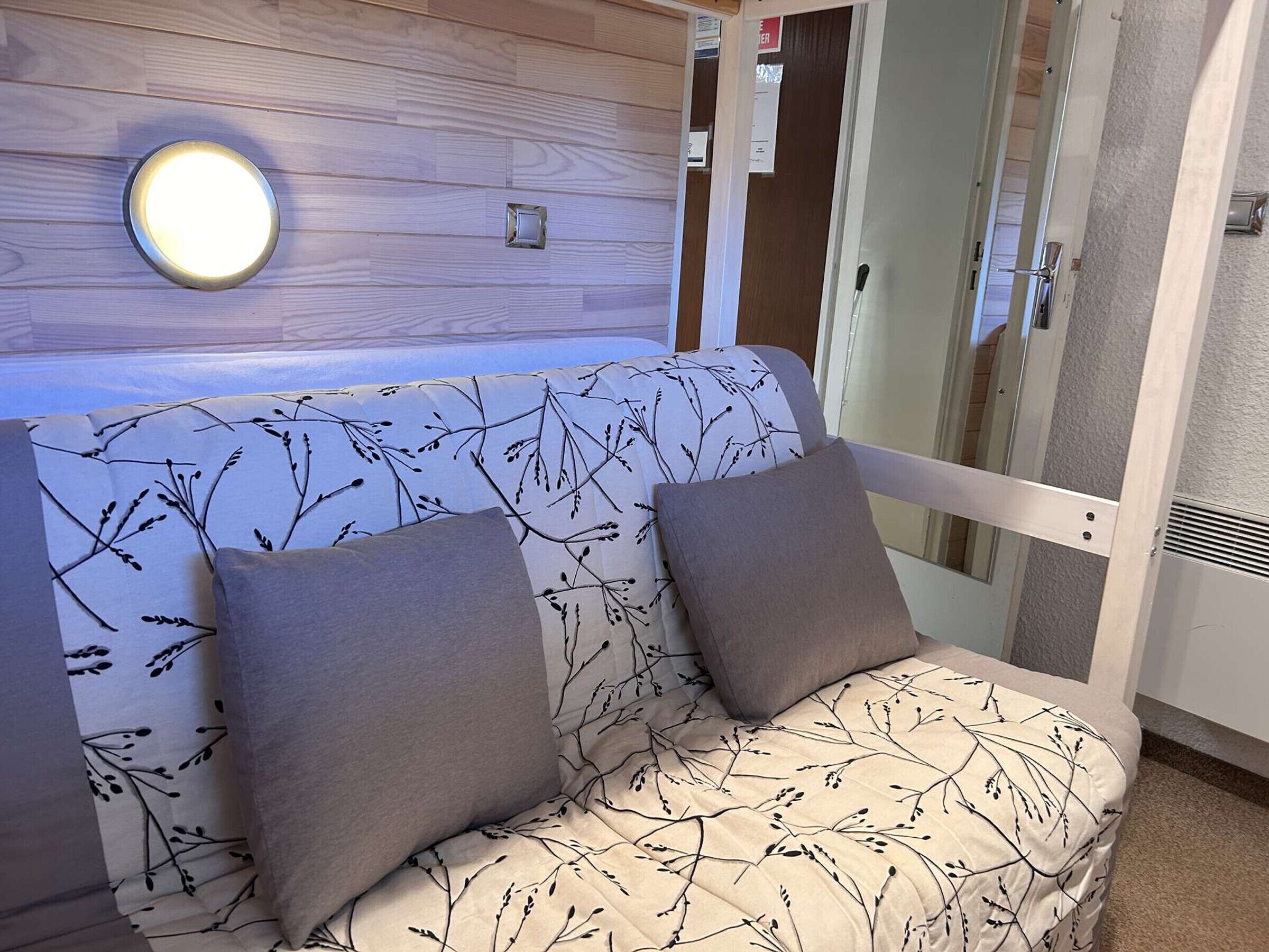 Een kamer met een bank tegen een muur, een ronde lamp en een deur met een ruit.