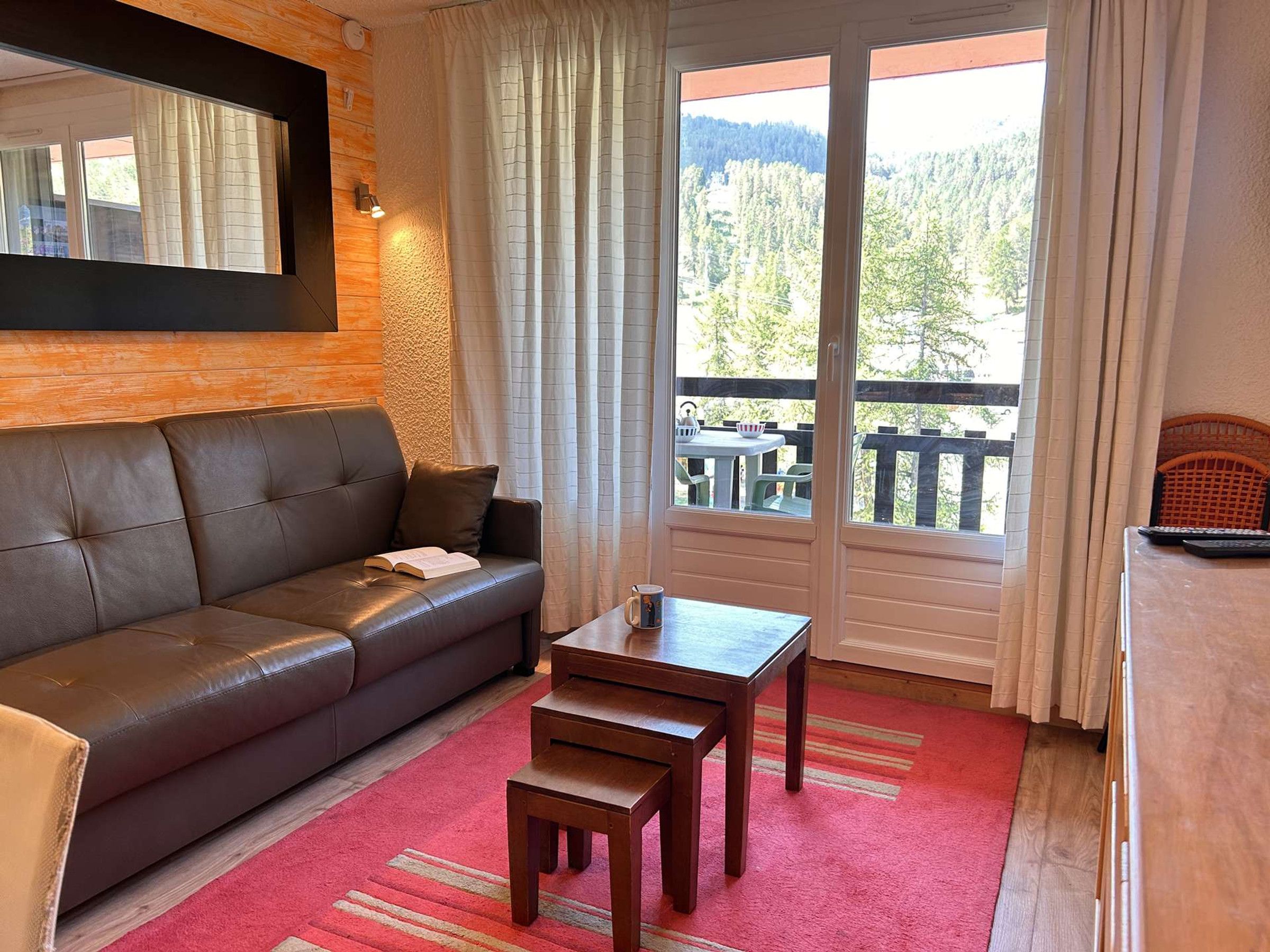 A living room with a leather sofa, a wooden coffee table, and a view of a balcony with outdoor furniture.