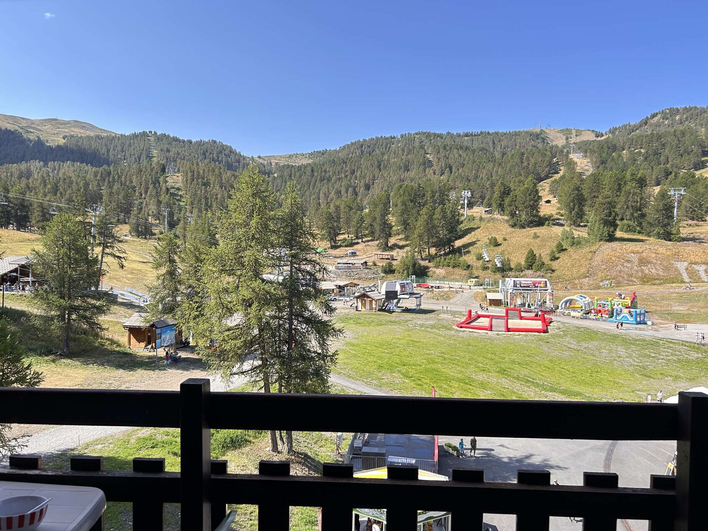 A mountainous landscape with a ski resort, including ski lifts, a red play structure, and a small building.