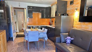 Ein modernes Wohnzimmer mit einem Ledersofa, einem Esstisch mit Stühlen sowie einer Küchenzeile mit Schränken und Geräten.