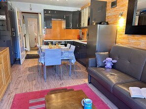 Ein modernes Wohnzimmer mit einem Ledersofa, einem Esstisch mit Stühlen sowie einer Küchenzeile mit Schränken und Geräten.