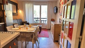 Ein Essbereich mit einem für vier Personen gedeckten Tisch, eine Küche mit Kühlschrank und ein Fenster mit Vorhängen.