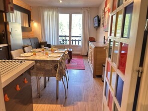 Ein Essbereich mit einem für vier Personen gedeckten Tisch, eine Küche mit Kühlschrank und ein Fenster mit Vorhängen.