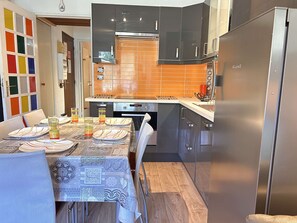 Eine moderne Küche mit Esstisch für vier Personen, einem Kühlschrank und einem Herd.