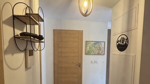 A hallway with a wooden door, a bench, a wall-mounted shelf, and a wall with a framed map and a circular emblem. - Contemporary apartment - 8 guests (Les Carroz d'Arâches)