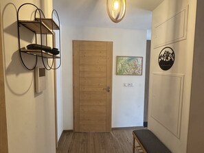 Ein Korridor mit einer Holztür, einer Bank, einem an der Wand befestigten Regal und einer Wand mit einer gerahmten Karte und einem runden Wappen.