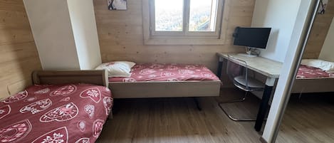 Una habitación con dos camas, un escritorio, una silla y una ventana.
