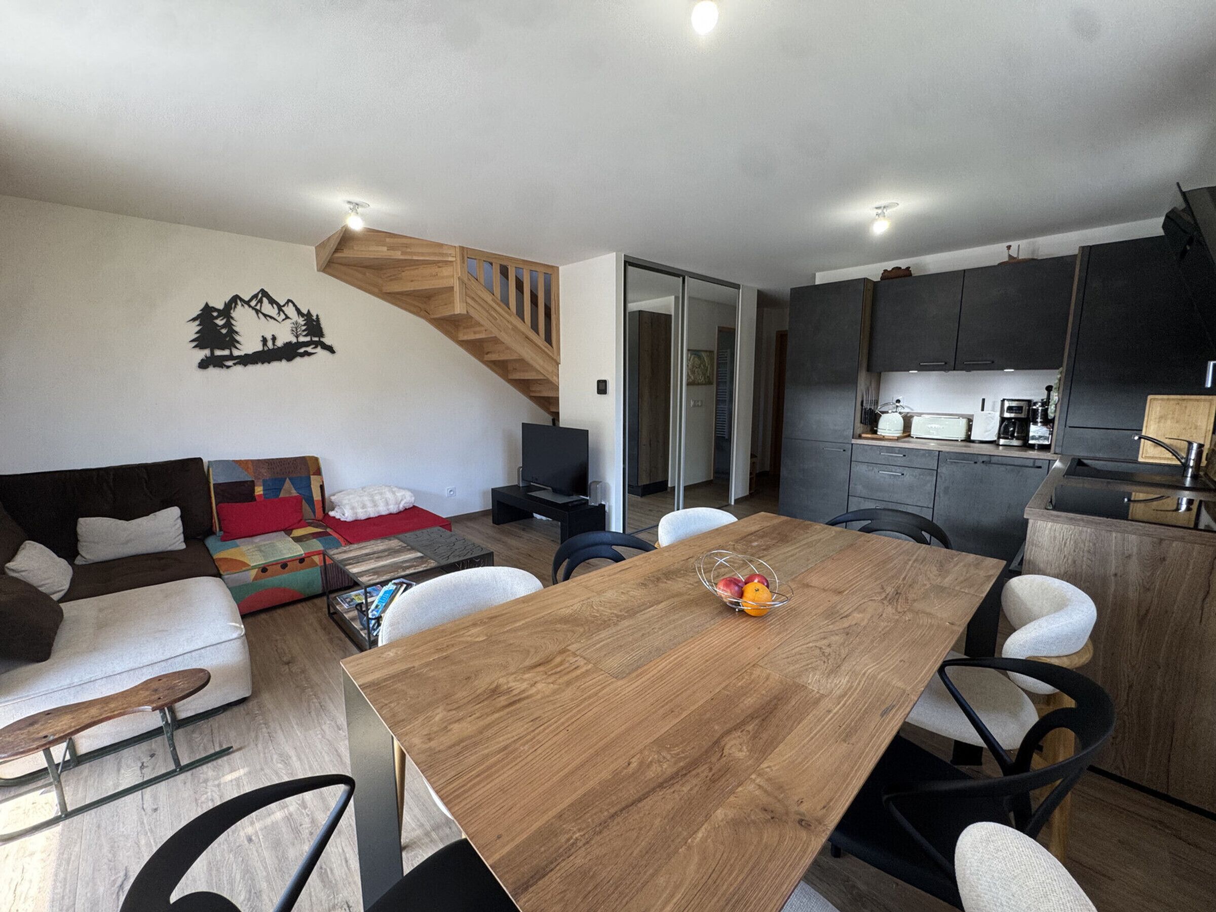 Un espace de vie moderne comprenant une table à manger en bois, un canapé, un téléviseur et un coin cuisine.