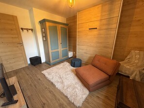 Ein Zimmer mit Holzschrank, Sofa, Teppich und kleinem Hocker.