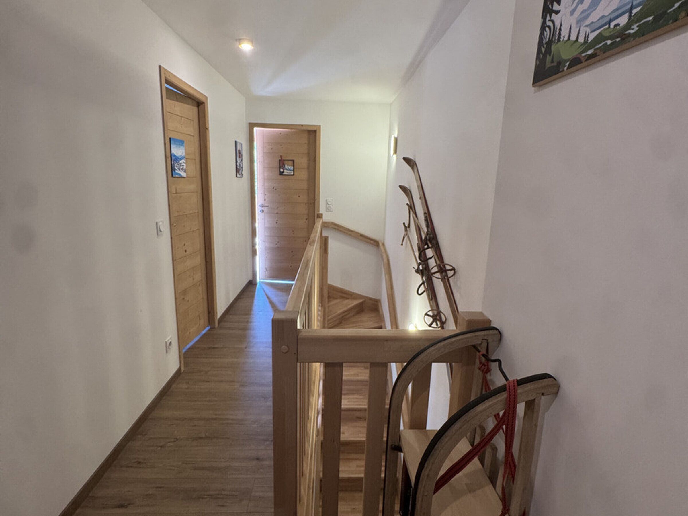 A hallway with wooden flooring, wooden doors, and a ski rack against the wall.