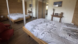 A bedroom with a large bed, a wooden floor, a red chair, a bedside table with a vase, and a mirror on the wall. - Contemporary apartment - 8 guests (Les Carroz d'Arâches)