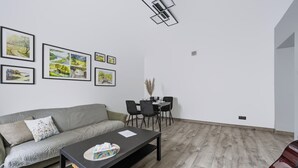 Ett modernt vardagsrum med en grå soffa, ett svart soffbord och en matplats med ett bord och stolar. Det finns inramade tavlor på väggen.