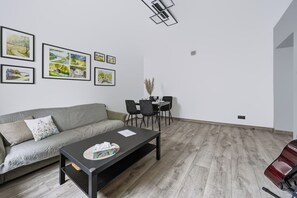 A modern living room with a grey sofa, a black coffee table, and a dining area with a table and chairs. There are framed pictures on the wall. - Warsaw Center Apt — Old Town Nearby, Workspace (Warszawa)