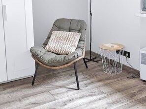 A wicker chair with a cushion and a small round table with a wireframe base. - Warsaw Center Apt — Old Town Nearby, Workspace (Warszawa)