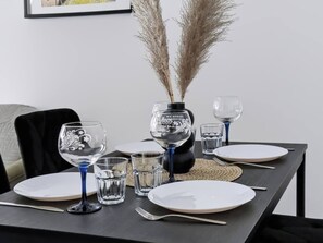 Ein Esstisch ist gedeckt mit weißen Tellern, blauem Glas und einer Dekovase mit Pampasgras.