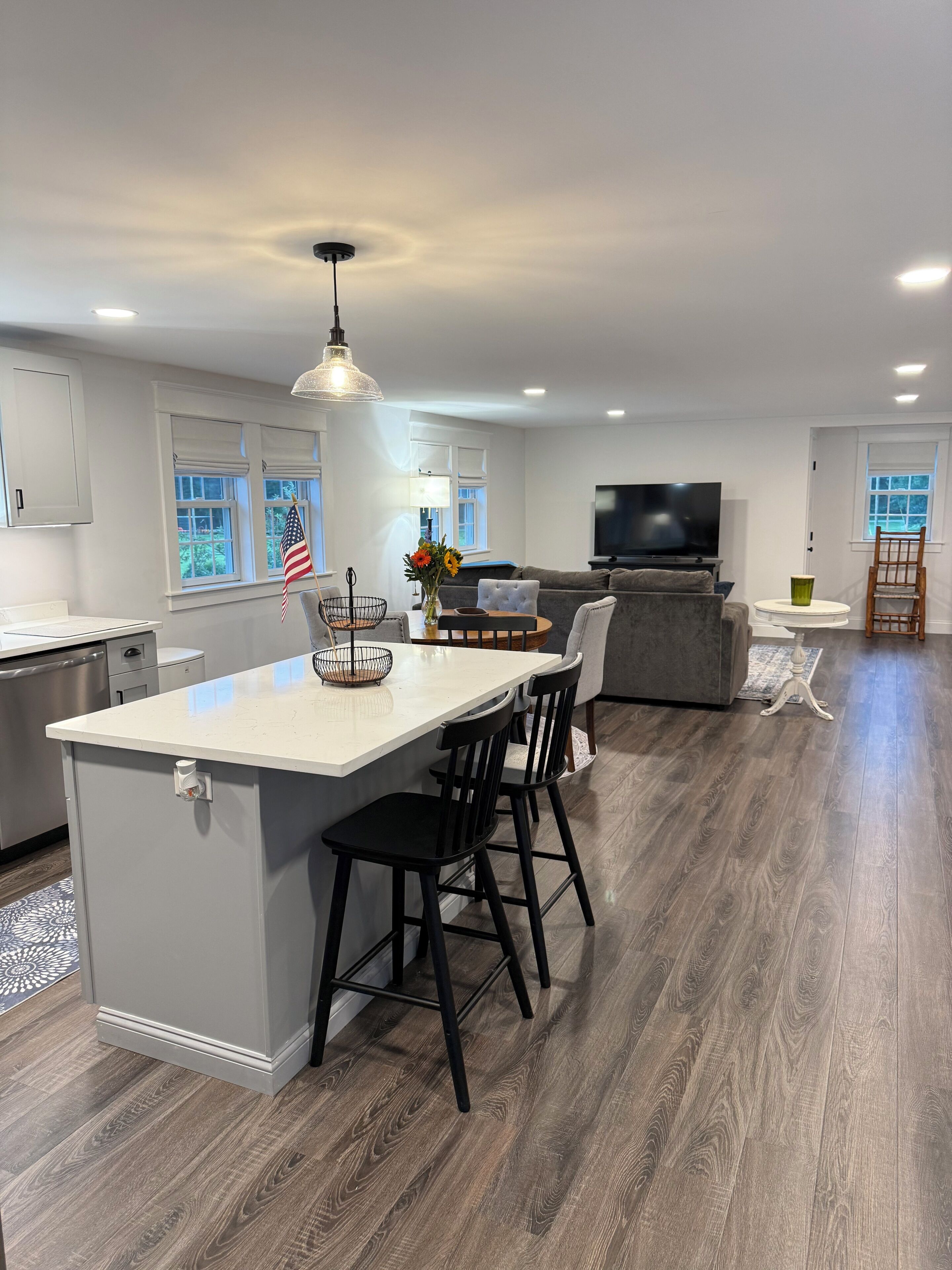 A modern kitchen with a central island, bar stools, a dining table, and a television in the living area.