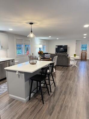 A modern kitchen with a central island, bar stools, a dining table, and a television in the living area. - Beautiful studio apartment with AC in South Kingstown, Rhode Island. (South Kingstown)