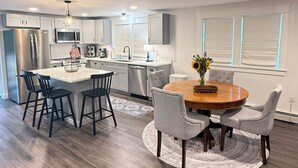 A modern kitchen with a central island, bar stools, and a dining table with chairs.