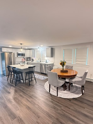 Una cocina moderna con una isla central, taburetes de bar y una mesa de comedor con sillas.
