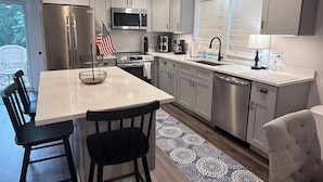 A modern kitchen with stainless steel appliances, a dining area with black chairs, and a patterned rug on the floor.