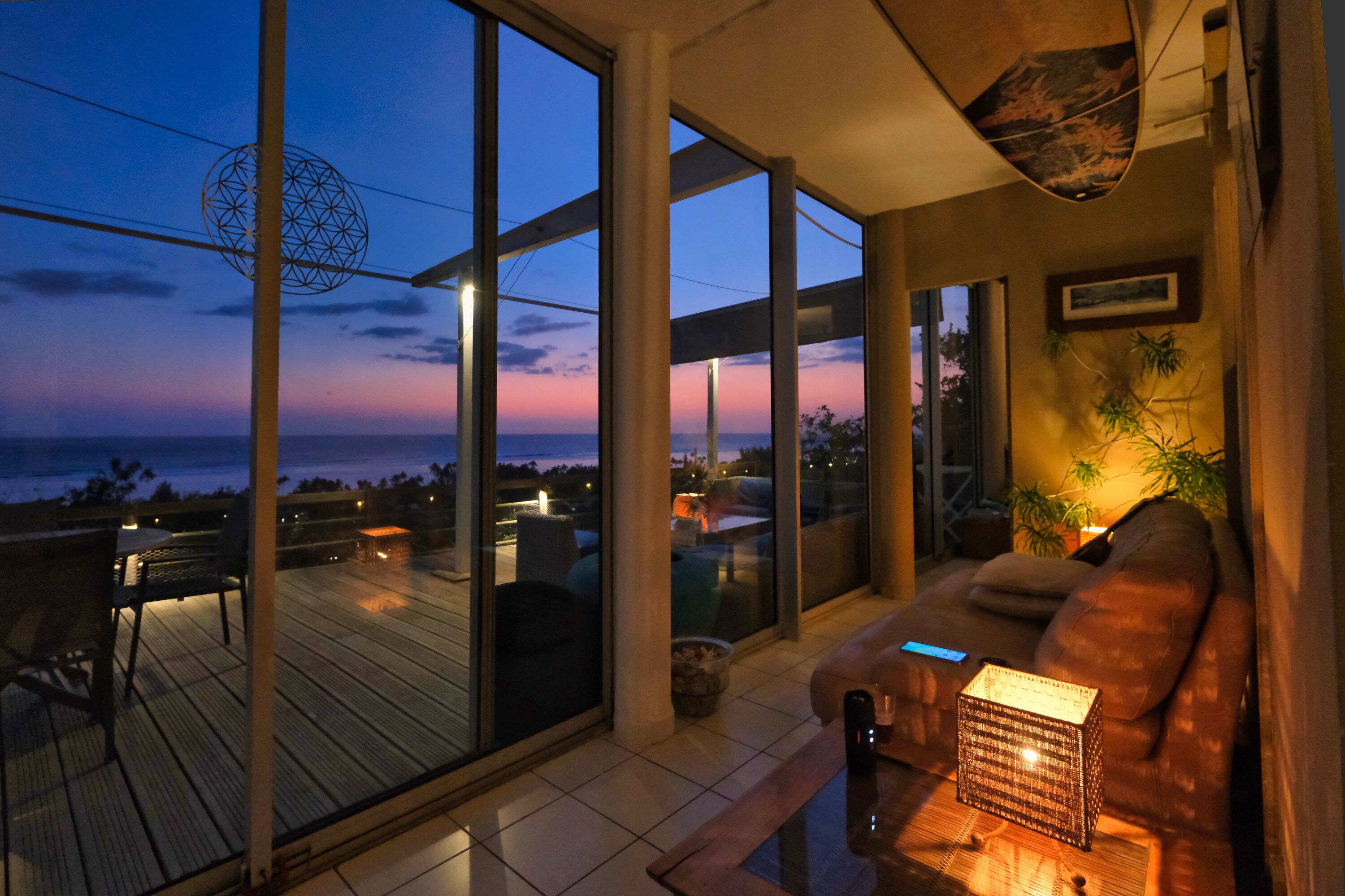 Un interior moderno con ventanas amplias, una terraza de madera y un área de descanso con mesa y sillas.