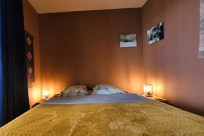 A single bed with a textured bedspread, two pillows, two bedside lamps, and a small framed picture on the wall. - Charming 100-square-meter apartment + 40-square-meter terrace with a stunning view of the sea and lagoon (Saint-Paul)