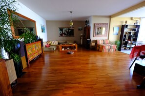 Ein großzügiges Wohnzimmer mit Holzdielenboden, einer Sofagarnitur, einem Couchtisch und einem Bücherregal.