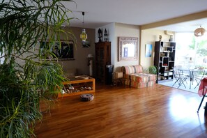 A living room with wooden flooring, a sofa, a coffee table, a bookshelf, and a dining area with a table and chairs. - Charming 100-square-meter apartment + 40-square-meter terrace with a stunning view of the sea and lagoon (Saint-Paul)