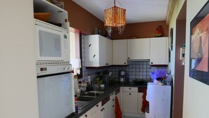Eine kompakte Küche mit weißen Schränken, einer Mikrowelle, einem Kühlschrank und einer Pendelleuchte.