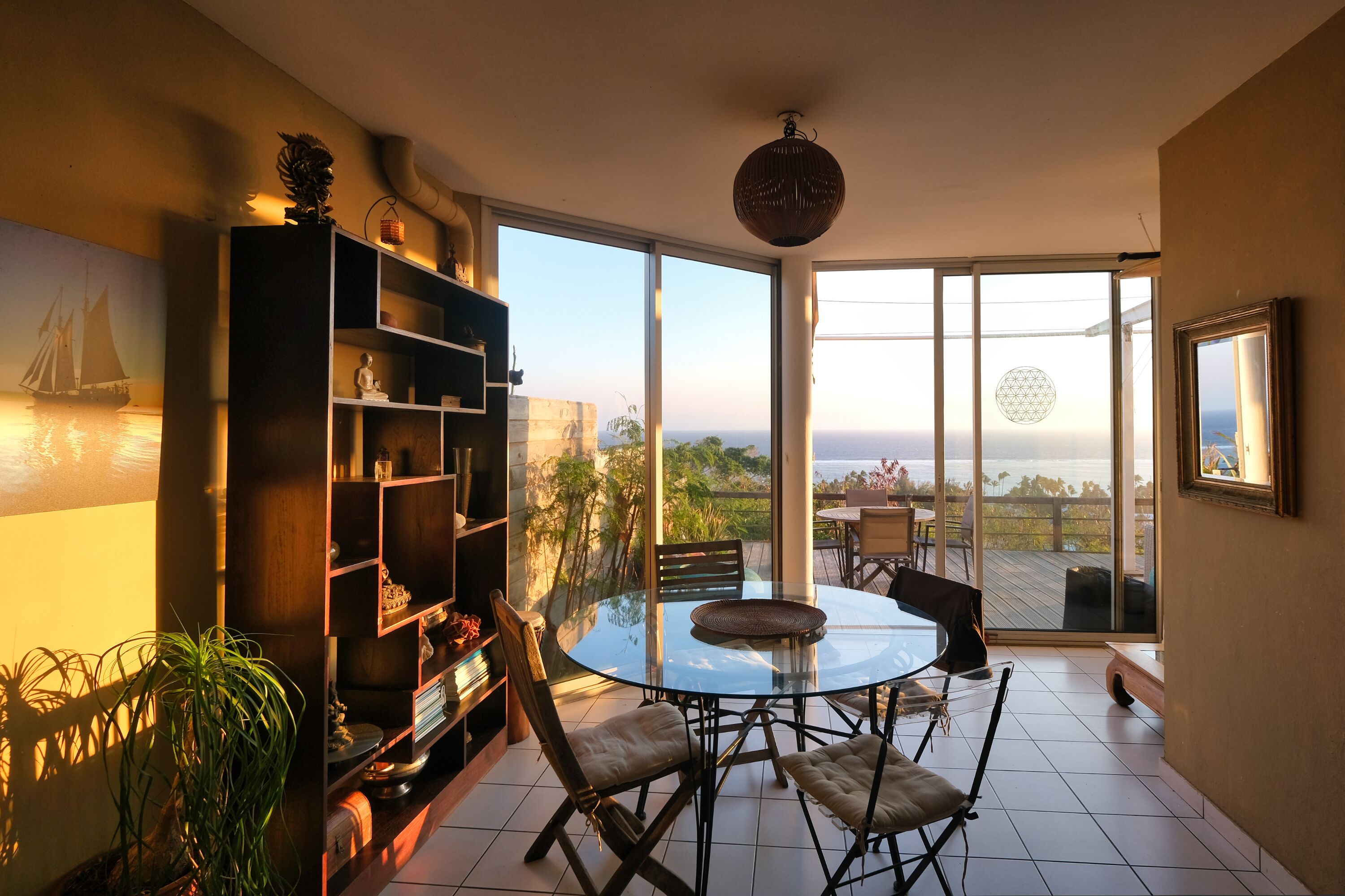 Una habitación con una mesa y sillas de vidrio, una estantería y vista al océano.