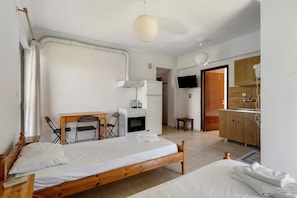 A room with a bed, a desk, a chair, a television, and a kitchenette.