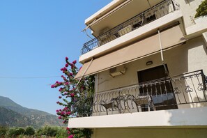 A multi-story building with balconies, a clear sky, and a mountainous landscape in the background. - Rousetis Two-Bedroom Apt 102 - 200m from the Sea (Aigialeia)