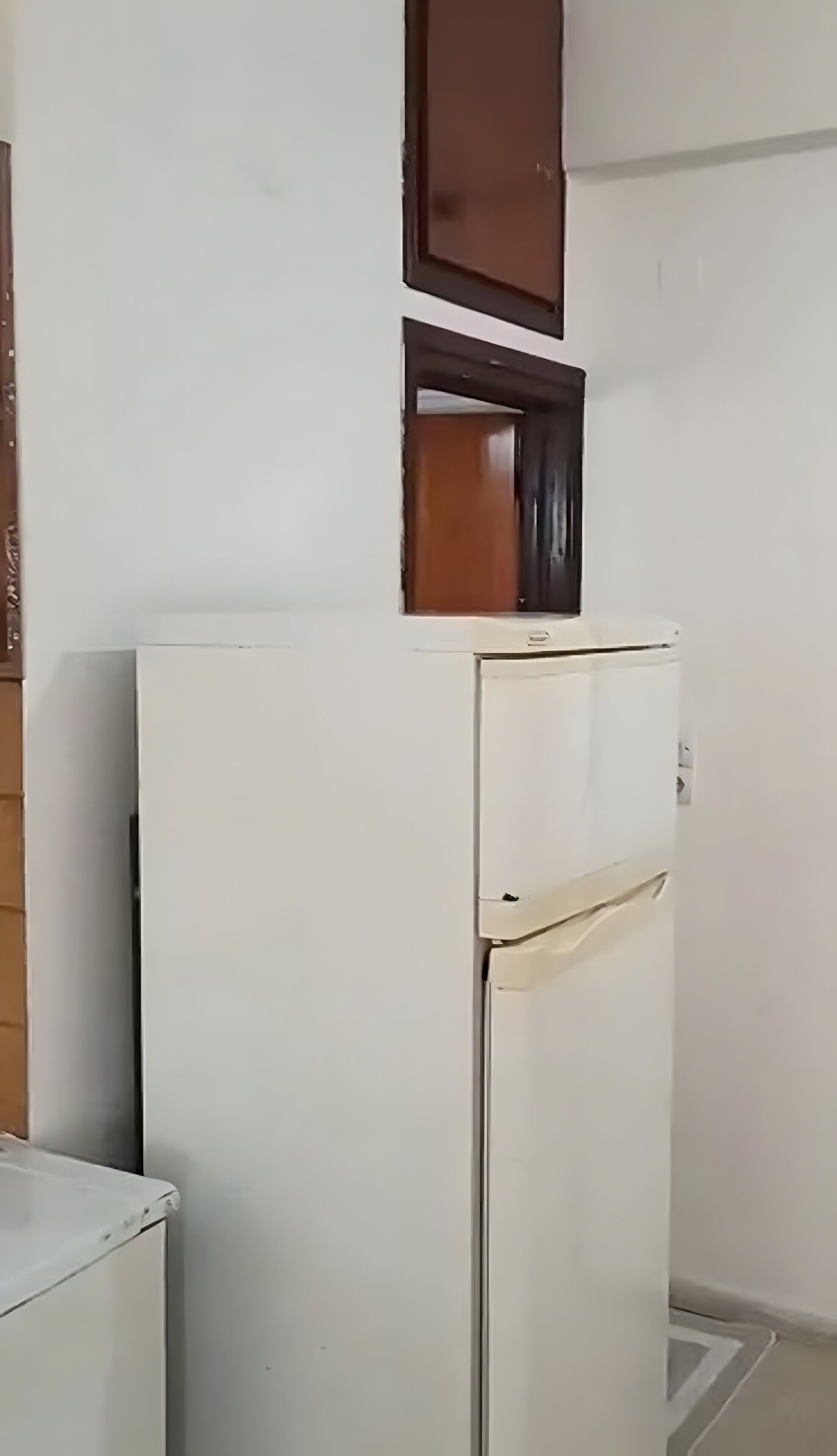 A white refrigerator in a room with a wooden cabinet above it.