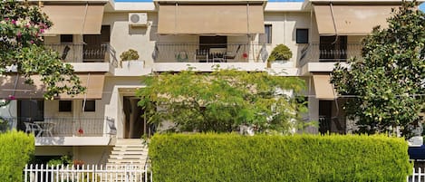 A multi-story residential building with balconies, a gated entrance, and a well-maintained hedge.