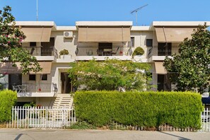 Un immeuble résidentiel à plusieurs étages, doté de balcons, d’une entrée sécurisée et d’une haie bien entretenue.