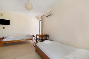 A room with two single beds, a wooden table with chairs, a television, and a ceiling fan. - Rousetis Two-Bedroom Apt 205 - 200m from the Sea (Aigialeia)