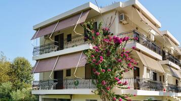 A multi-story residential building with balconies, awnings, and a flowering tree.