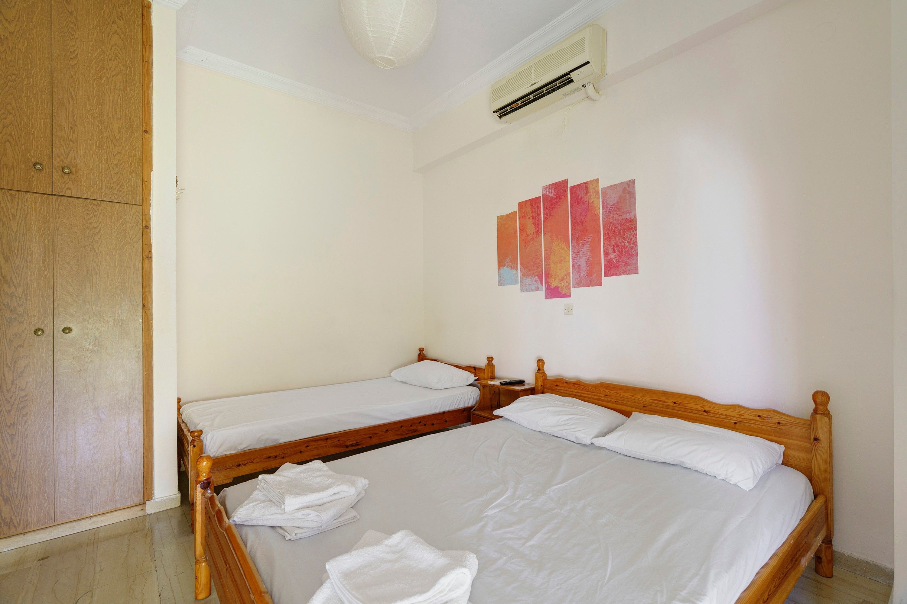 A hotel room with two wooden beds, a wardrobe, a ceiling fan, and a wall-mounted air conditioner.