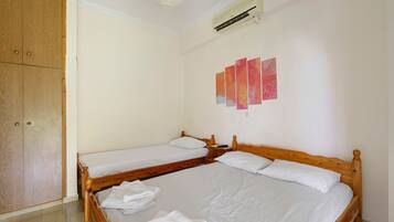 A hotel room with two wooden beds, a wardrobe, a ceiling fan, and a wall-mounted air conditioner.