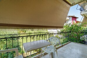 A balcony with a table and chairs, a metal railing, and a view of greenery and buildings.