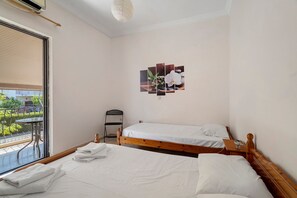 A hotel room with two beds, a small table, a chair, and a window with a view of greenery. - Rousetis Studio 104 - 200m from the Sea in Aígio (Aigialeia)