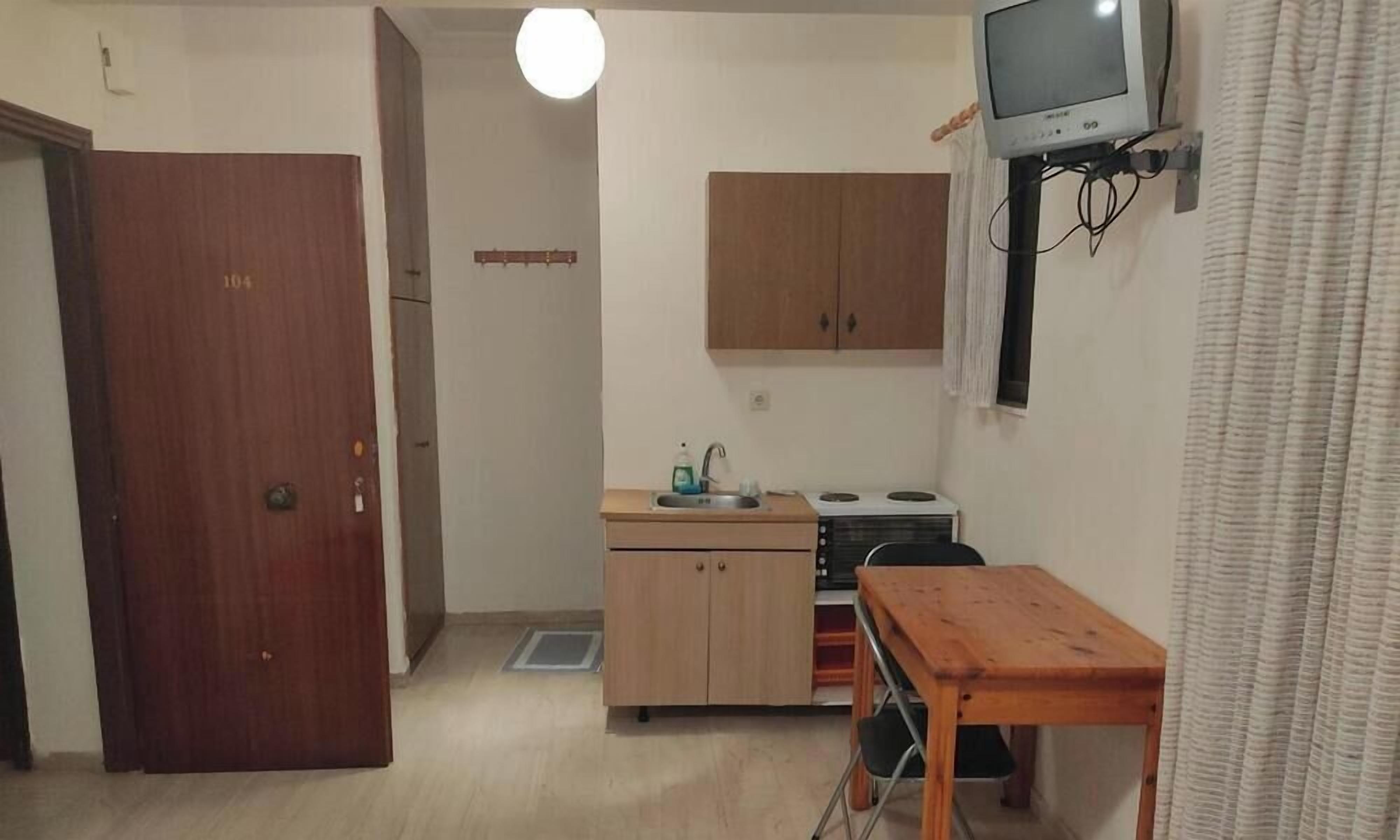Ett kompakt kök med ett träskåp, ett litet bord och en tv som är monterad på väggen.